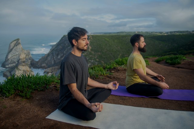 Two people meditating outdoors on mats above the coast