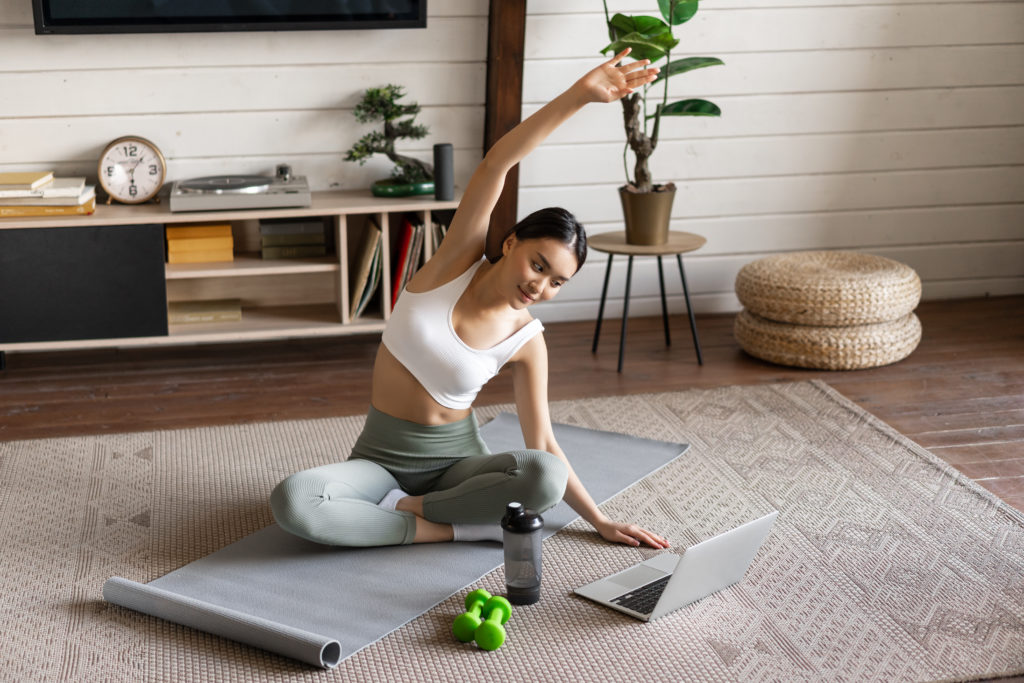 Lernen Sie Pilates Christoph Klaus-Onlineplattform kennen! 3 young asian fitness girl doing stretching sport workout home stretch arms looking laptop f